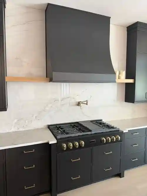 Black kitchen cabinetry with slab backsplash and brass details by Braga Remodeling