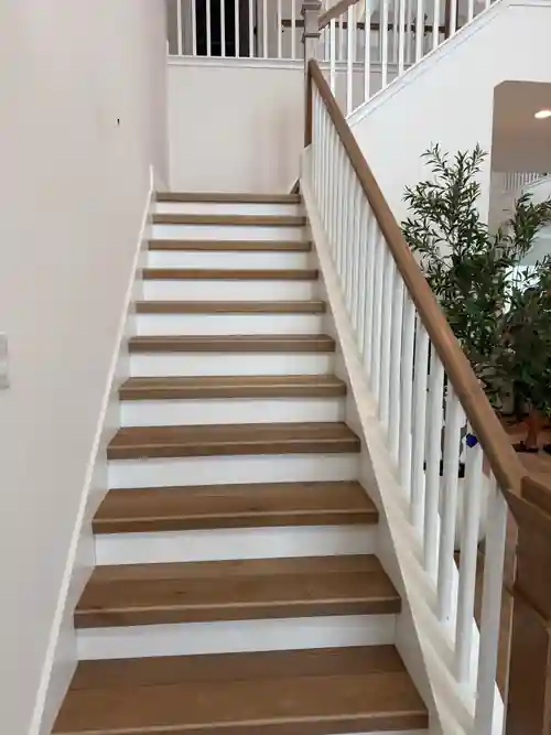 Finished wood staircase with white balusters completed by Braga Remodeling
