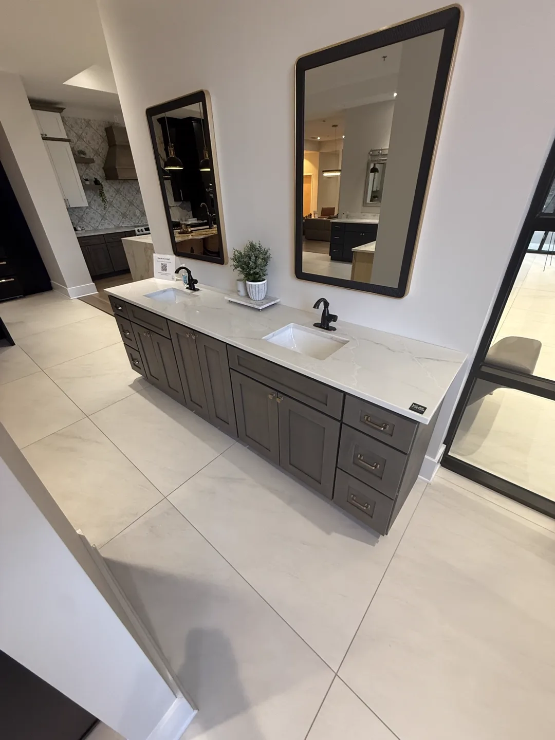 Double vanity in dark gray cabinets with white marble-look top and framed mirrors — design idea from a supplier showroom