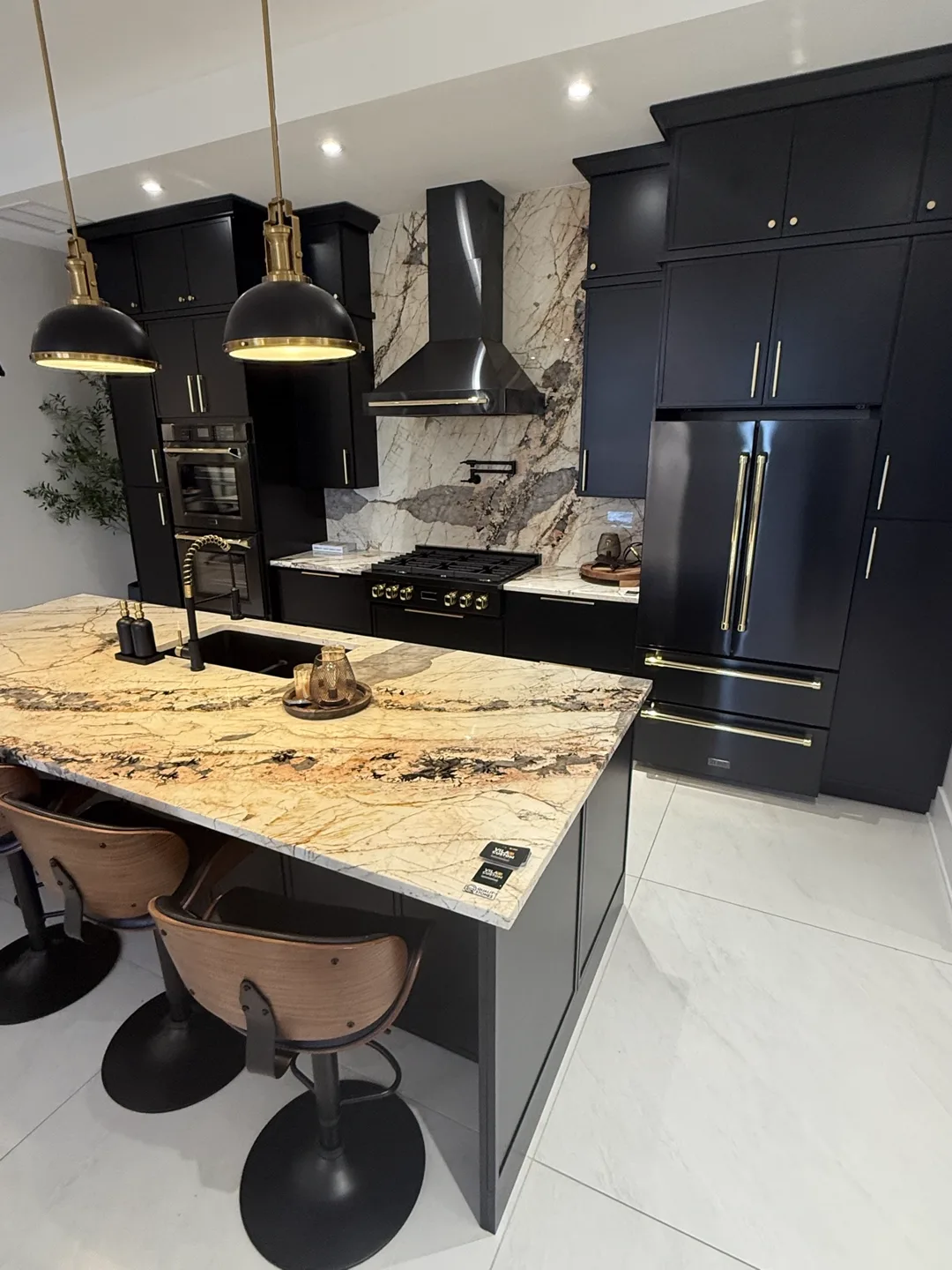 Black shaker kitchen cabinets with brass hardware, marble-look island and slab backsplash — design idea from a supplier showroom