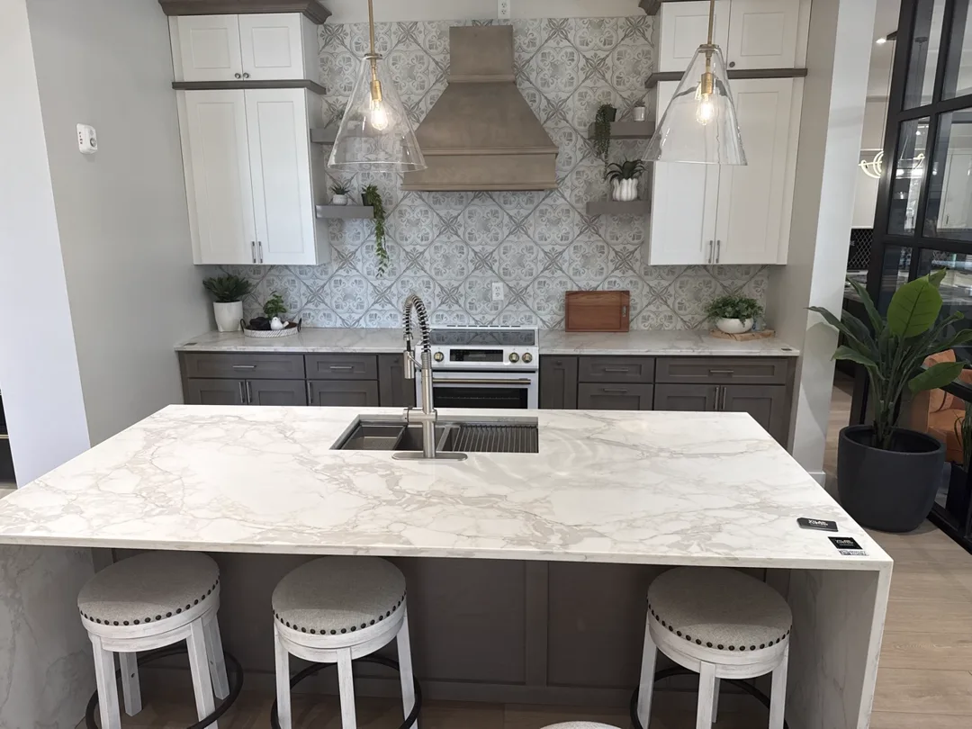 Gray and white kitchen with waterfall island, patterned tile backsplash and glass pendants — design idea from a supplier showroom