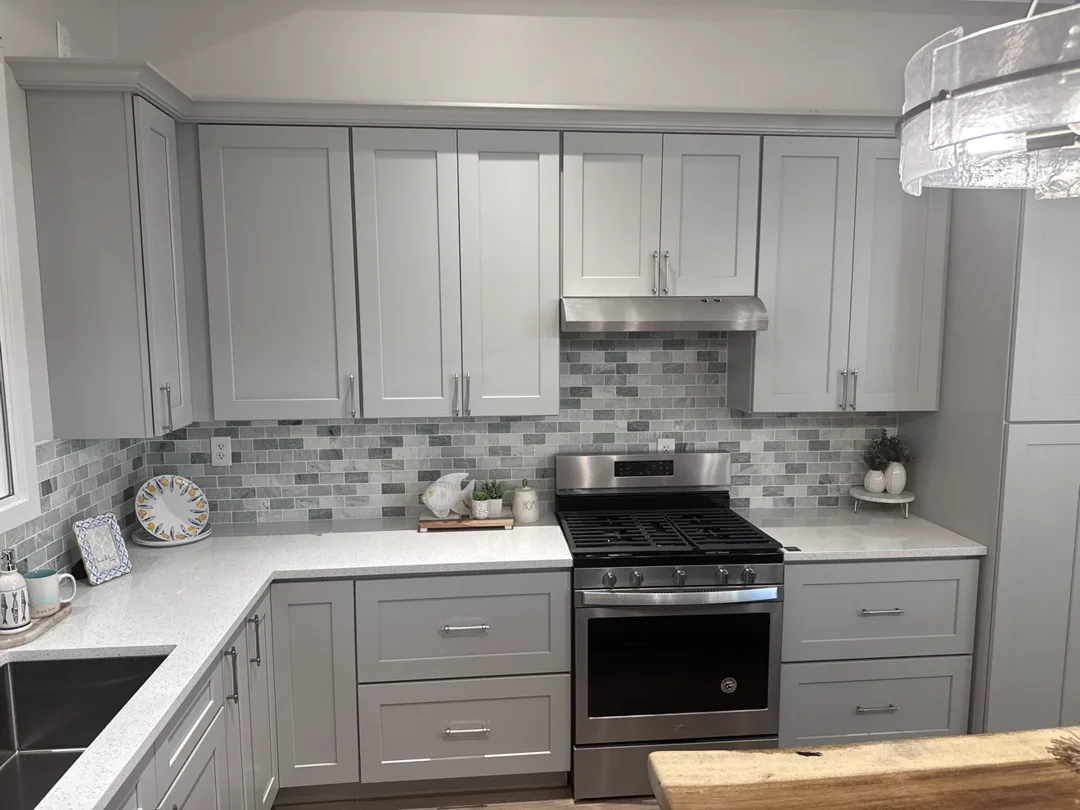 Natural wood upper cabinets with dark green base cabinets, vertical green tile backsplash and marble counters — design idea from a supplier showroom